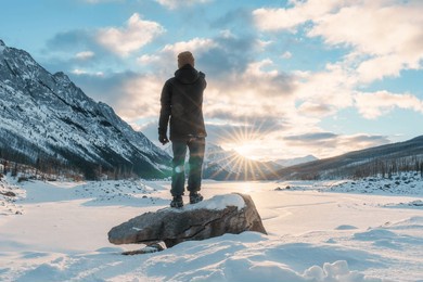 rear view of adventurer man standing and pointing towards the rocky mountains and frozen lake in winter at medicine lake, alberta, canada