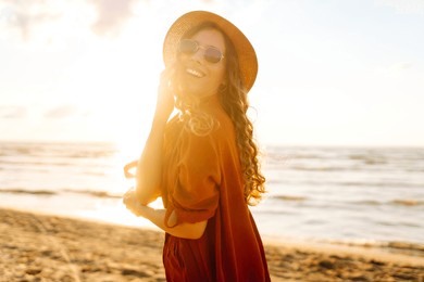 a young woman stands on the beach at sunset, gently touching her hair while basking in the warm glow of the sun. lifestyle, tourism, nature, active life.