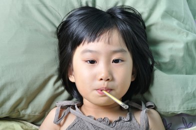 little asian sick girl under blanket with temperature in mouth