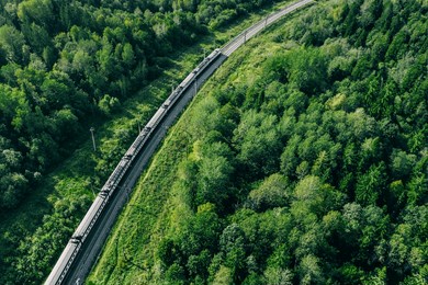 aerial drone view of train in beautiful green summer forest. long commuter train moving to railway station