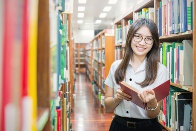 asian student in uniform reading in the library at university