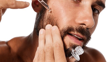 cropped portrait of handsome young man taking care after beard, applying moisturizing serum isolated on white studio background. concept of male beauty, skin care, hygiene, health, cosmetics
