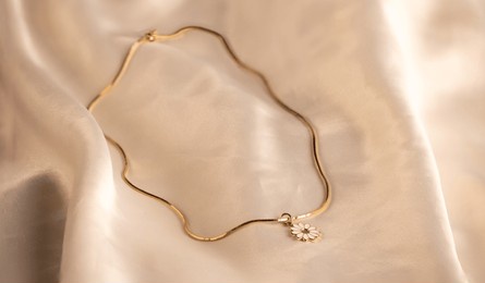 gold necklace with white flower charm on it on white silk background
