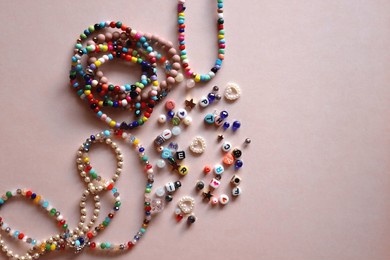 colorful diy necklaces, friendship bracelets and various plastic beads on pastel pink background. flat lay.
