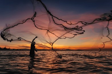 silhouette of traditional fishermen throwing net fishing during sunset. located at terengganu, malaysia.