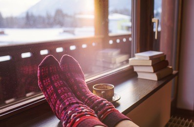 feet in woollen socks by the alps mountains view. woman relaxes by mountain view with a cup of hot drink. close up on feet. winter and christmas holidays concept.