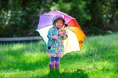 funny cute toddler girl wearing waterproof coat with colorful umbrella playing in the garden by rainy and sunny day