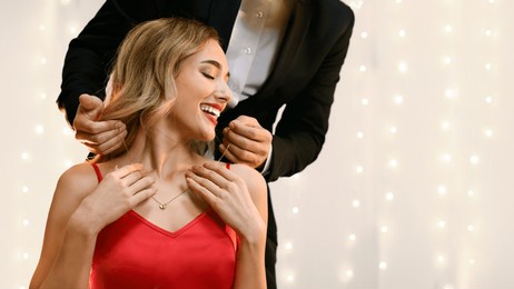 anniversary gift. affectionate man presenting golden necklace to his pleased girlfriend at romantic dinner in restaurant, copy space