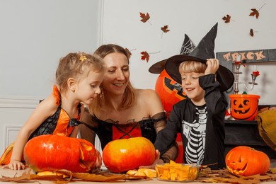 mother and two children, boy, girl laughing make funny pumpkin decorations, participate in a halloween activity in living room