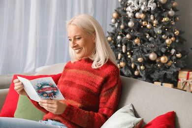 mature woman reading greeting card for christmas celebration on sofa at home
