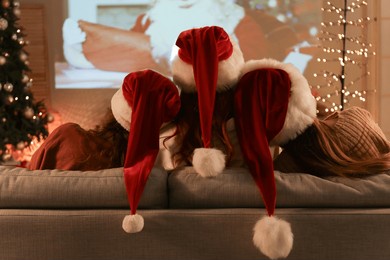 young women in santa hats watching christmas movie on projector screen at home, back view