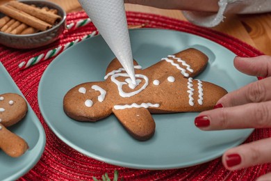 making christmas cookies - gingerbread men,  a woman is decorating cookies with royal icing.