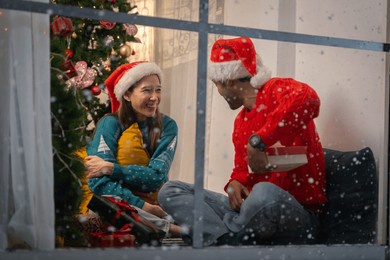 asian couple doing activities together at home by the window, outside the house, snow is falling on christmas day.