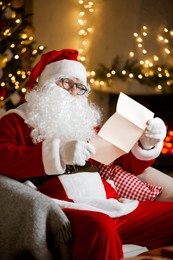 jolly santa claus with eyeglasses reads heartfelt letters by a cozy fireplace, filled with warmth and cheer in a cozy festive room with christmas tree, decorated by twinkling lights. holiday vibes