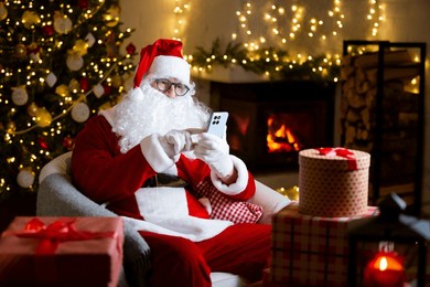 jolly santa claus with eyeglasses scrolls his smartphone, reads heartfelt letters by a cozy fireplace in a cozy festive room with christmas tree, decorated by twinkling lights. coming holiday vibes