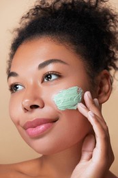 skin care dermatology treatment routine. young african american woman smiling, applying a green skincare clay face mask smear , with natural curly hair, close-up beauty shot. 