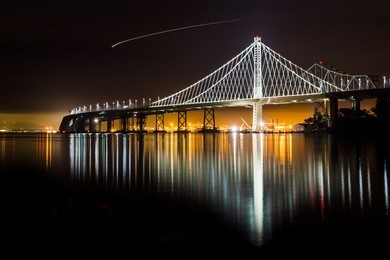beautiful new east span bay bridge at night illuminated reflecting oakland port color lights cityscape. the iconic and majestic bridge after dark long exposure in san francisco greets traveler.