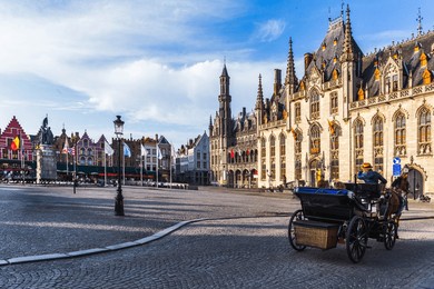 horse-drawn carriage with tourists in grote markt and empty square, brugge, flanders in belgium.