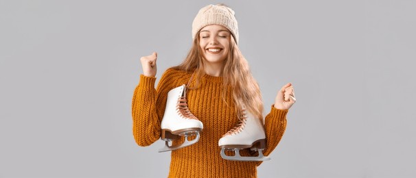 happy young woman in warm sweater and with ice skates on grey background