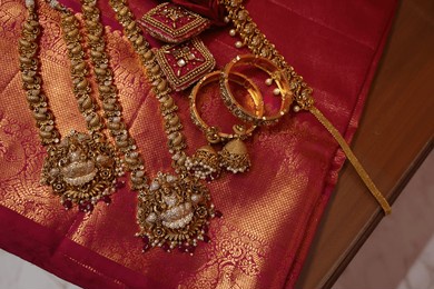 multiple gold chain and necklaces placed on red silk saree. indian bridal gold jewelry collection. antique gold jewels