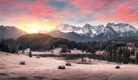 magical sunrise scenery with mountains, illuminated clouds, a scenic lake and woods on hills in the alps, frozen meadow and cabins. beautiful nature in germany.
