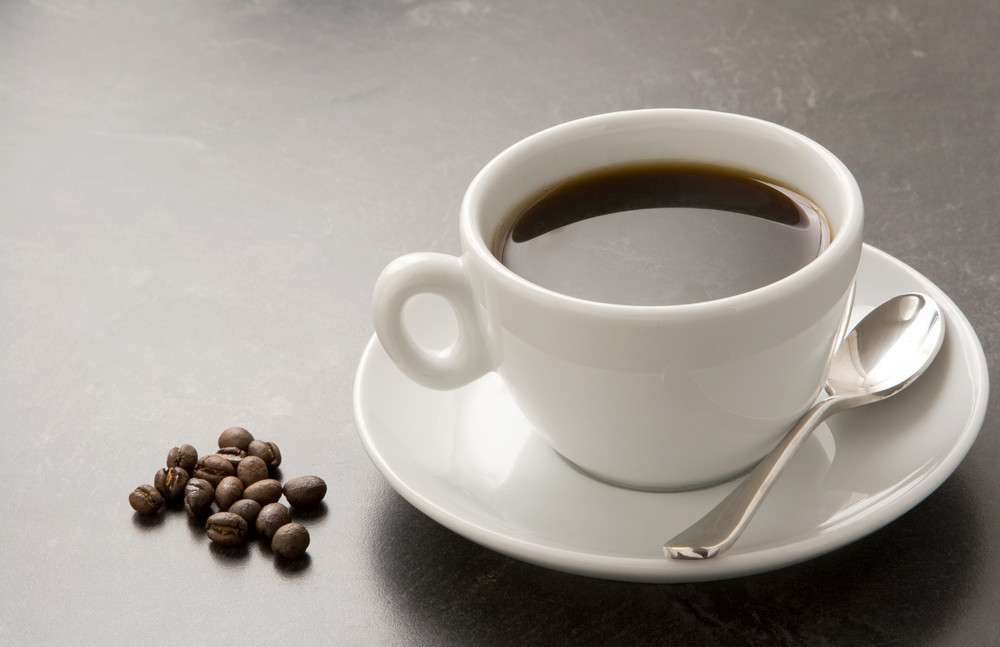 white coffee cup and saucer on black table with whole beans.