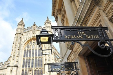 view of the entrance of the historic roman baths with bath abbey in the background in the historic somerset city of bath in england