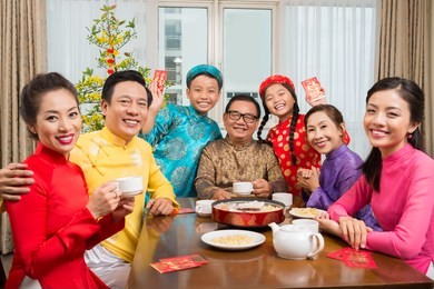 happy big vietnamese family in traditional costumes sitting at table and looking at the camera
