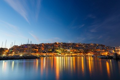 typical colorful evening scenery in the mikrolimano marina in athens in the afternoon, with clouds over the city lights and many restaurants on the seafront in greece long exposure photography