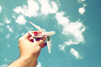close up photo of man's hand holding toy airplane against blue sky with clouds