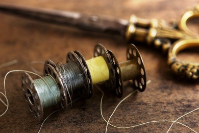 vintage sewing machine bobbins with vintage gold ( brass ) scissors on a old grungy work table. tailor's work table. textile or fine cloth making. shallow depth of field.