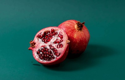 whole and cut pomegranate with red juicy seeds displayed on a green surface. high-quality horizontal food image for health and nutrition concepts