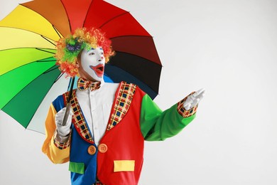 emotional clown with colorful umbrella on light background, space for text