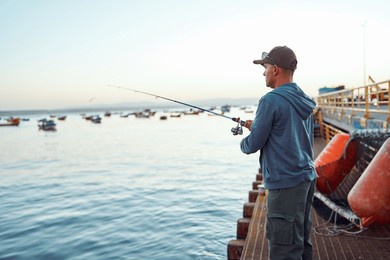 fisherman casting fishing rod from pier at sunset with boats in background in tongoy, coquimbo region, 