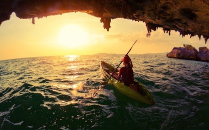 young lady paddling the kayak from limestone cave towards open sea