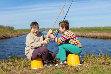 the boys are friends on a fishing trip by the river eating a bun and laughing. children are friends on a summer fishing trip.