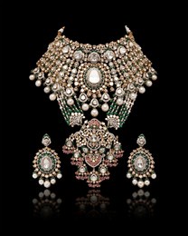a beautiful golden necklace and earrings with green emerald stones, ruby, pearls and diamonds, on a black background.