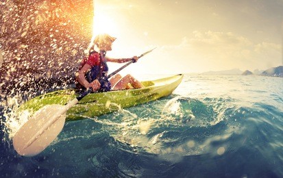 young lady paddling hard the kayak with lots of splashes near the cliff at sunny day