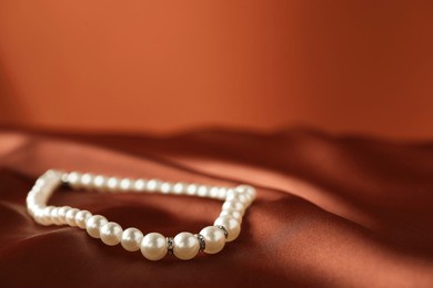 beautiful pearl necklace on brown silk, closeup. space for text