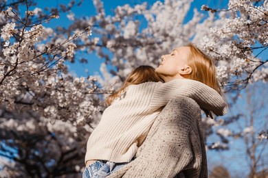 mother and daughter are happy together in blooming trees garden at spring in sunlight. woman mom and girl playing, dancing and hugging outdoors. happy mother's day! family holiday and togetherness.