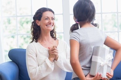 cute girl offering gift to her mother in the living room