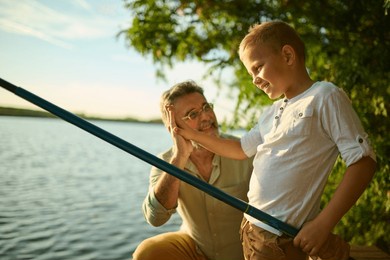 grandfather and grandson fishing by a tranquil lake, enjoying nature and creating memories. high fiving in golden sunlight, cherishing togetherness