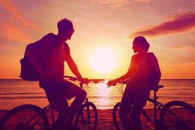 couple tourists with bicycles watching sunset. summer nature background with beautiful sky and sea. active leisure concept.