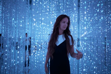 a woman exploring the mesmerizing blue light installation at teamlab tokyo, surrounded by glowing led strands and reflections. 