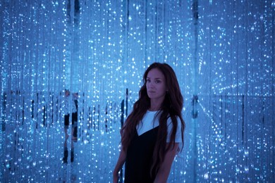 a woman standing in a glowing blue led light installation at teamlab tokyo, surrounded by immersive and interactive digital art.