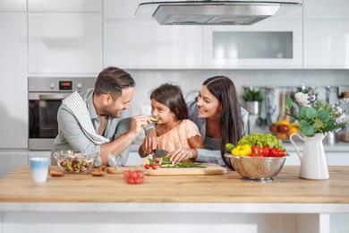 a cheerful family makes a healthy meal in their bright, modern kitchen. they chop vegetables, share smiles, and embrace quality time together while cooking.
