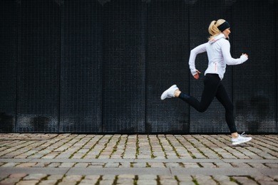 view of young woman running on sidewalk in morning. health conscious concept with copy space.