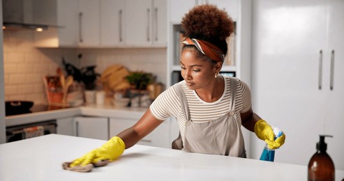 woman, cloth and wipe on kitchen counter for hygiene with spray, gloves or chemical for shine in home. african person, cleaning and bottle for dust, dirt or bacteria with sanitation liquid in house