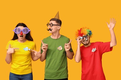 young surprised friends in funny disguise with paper fishes on yellow background. april fool's day celebration