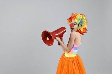 girl dressed like clown with megaphone on grey background, space for text. surprise party